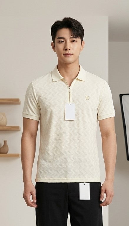 A man wearing a cream-colored short-sleeve polo shirt with a subtle textured pattern and a small embroidered logo on the chest, paired with black pants. The shirt has a white hangtag attached.